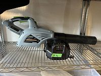 Side view of EGO leaf blower body and included charger on metal shelf