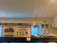 AeroGarden Elite grow system box and metal oil/vinegar set on shelf.