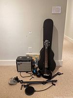 Overview of both guitars, amp, case, headphones and mic stand on beige carpet against wall
