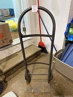 Front view of black steel hand truck showing handle and base with rust.