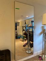 Full-length rectangular wall mirror with thin metal frame leaning against a white wall, reflecting a room interior