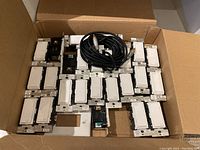 Cardboard box containing twenty-two white Leviton Decora Smart Wi-Fi switches and two coiled black cables with connectors.