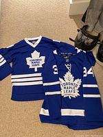Two blue Toronto Maple Leafs kids hockey jerseys laid flat showing front side with white maple leaf logos and numbers 34 on one jersey.