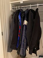 8 men's jackets hanging on a rod in a closet