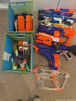 Overview of Nerf blasters, accessories including multiple orange magazines and two fabric storage bins