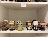 Front view of 6 Star Wars Funko Pop figures on shelf: a mustard-brown character, two figures with goggles, Jabba the Hutt, Princess Leia, scout trooper, and Han Solo.