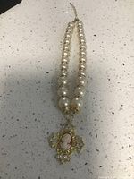 Full view of the pearl necklace with the cameo cross pendant displayed flat on a countertop showing the overall design and chain.