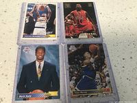 Four basketball player cards displayed on a white marble surface showing front faces of cards with different players in various poses.