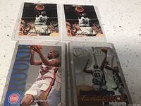 Four basketball cards: two identical Tim Duncan cards in black/white uniform jumping, one Grant Hill rookie card in Detroit Pistons uniform, one Tim Duncan Vault Matrix card grayscale
