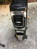 Front view of black Honeywell oil-filled radiator heater showing digital display, control buttons, and missing front wheel.