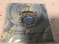 Photo of the Smithsonian Hope Diamond Pin in original clear plastic packaging with museum card insert showing pin on a blue background.
