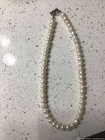 Front view of a white pearl necklace laid out on a speckled countertop showing the entire length and the clasp at one end.