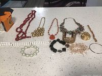 Full lot of assorted jewelry arranged on white speckled countertop including multiple necklaces, bracelets, and a brooch
