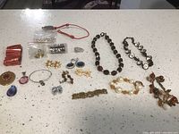 Wide shot of mixed jewelry lot spread on white speckled countertop including necklaces, bracelets, earrings, pins, and loose beads.