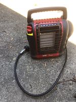 Front view of the red and black Mr Buddy propane space heater with attached flexible hose lying on concrete surface.