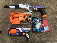 Four Nerf toy guns and a bag of Nerf Elite darts with clip all laid on concrete ground.