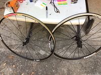 Two black alloy Oval bike tire wheel frames with multiple spokes leaning against a table outside.