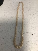 Full-length view of the pearl necklace laid out on a speckled countertop, showing the pearls' gradual size variation.