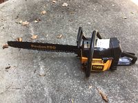 Side view of Poulan 330 Pro chainsaw showing yellow and black body and metal cutting bar with chain, on concrete ground with dry leaves.