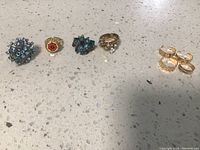 Lot of six rings and toe rings placed on a white speckled surface, showing size and design variety.
