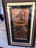 Front view of framed copper relief artwork depicting detailed scenes and signed by artist.