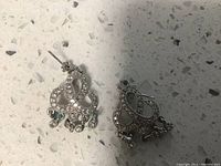Close-up photo showing pair of sterling silver earrings with decorative stones and fish-shaped charms hanging. Both earrings have 9.25 silver mark visible.