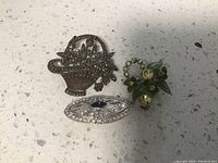 Three vintage pins: basket-shaped with flower stones, silver-toned oval with blue and clear stones, green-toned floral with leaf details