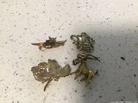 Four vintage pins on a speckled surface showing different styles and materials, including leaf and animal motifs.