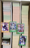 Top view of three vertical stacks of 1988 Score baseball cards inside a cardboard box with four cards displayed on top showing players in action.