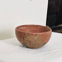 Side view of the red-brown pottery bowl showing its rounded shape and surface wear consistent with age.
