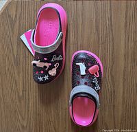 Pink Barbie Crocs with original tags, showing Barbie-themed charms and pink interior.