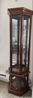 Full height view of curio cabinet showing wood frame, glass panels, glass shelves inside, and lower cabinet compartment with glass door panel.