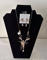 Photo of gold tone flower necklace and matching earrings displayed on a black necklace bust, showing intricate flower and leaf design.