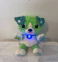 Front view of LeapFrog My Pal Scott green and white plush dog with glowing blue light on chest labeled 'Scout'