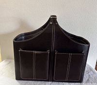 Front view of dark brown leather tote bag showing two exterior pockets and top strap with buckle.