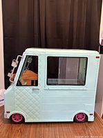 Side view of light blue Our Generation doll ice cream truck showing closed side window and pink wheels.