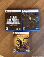 Front cover photo showing Alan Wake Remastered, The Callisto Protocol Day One Edition, and Mortal Kombat 11 Ultimate PS5 game cases on wooden floor.
