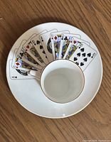Coffee cup on a ceramic plate featuring a fan of playing cards design with gold trim, showing Ace to Jack cards