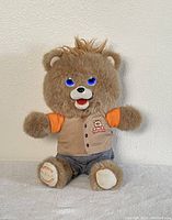 Teddy Ruxpin plush bear sitting upright, showing front view with lit-up blue eyes and mouth open.