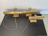 Two brass art picture lamps side by side, showing both lamps and their bases with attached wires.