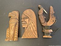 Three carved cedar figures displayed on black surface, showing front views of carvings.