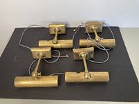 Four brass art wall lamps with wiring for LED conversion displayed on black surface.