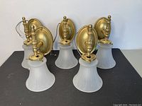 Five brass wall sconces grouped together showing front and side views. Each sconce has a round brass backplate and frosted ribbed glass bell-shaped shade. Wires visible for LED conversion.