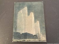 Front cover of the antique book shows stylized illustration of the Rockefeller Center skyscrapers against a muted background.