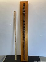 Full length of the 43-inch tall carved talking stick mounted on a wooden board with a measuring stick for scale.
