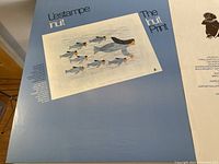 Poster with text 'L'estampe inuit The Inuit Print' showing art of swimming seals and birds in muted colors on a pale background with blue border