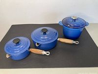 Three cobalt blue enameled cast iron cookware pieces arranged on black background.