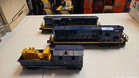 Three Lionel model trains displayed on a table including one caboose style and two diesel style engines, all in blue Chesapeake & Ohio livery.