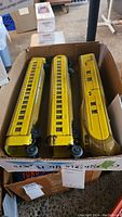 Box containing three yellow pre-war Lionel Union Pacific train cars, showing length and window details. Cars exhibit wear and paint chips on yellow surface.