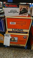 Stack of three boxed Lionel model train sets labeled Operating Santa Hand Car, Naughty & Nice Hopper 2 Pack, and Nutcracker Auto Gateman